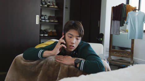 Asiatischer-Junge,-Der-Zu-Hause-Auf-Der-Couch-Liegt-Und-Mit-Dem-Smartphone-Spricht