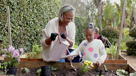 Happy-african-american-grandmother-and-granddaughter-watering-flowers-in-garden,-slow-motion