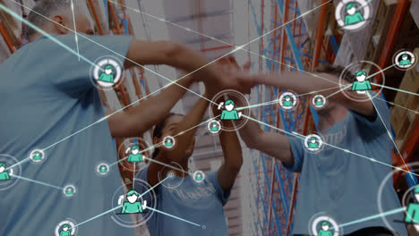 Animation-of-network-of-connections-with-icons-over-diverse-volunteers-stacking-hands-in-warehouse