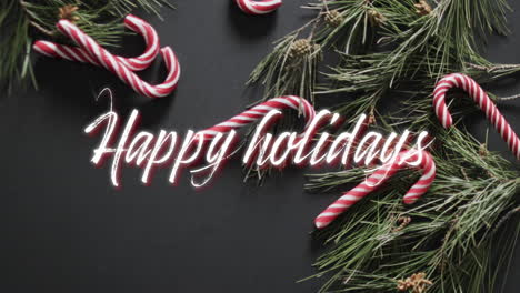 Happy-holidays-text-in-white-over-christmas-tree-sprigs-and-candy-canes-on-black