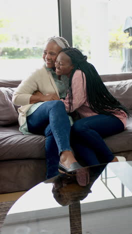 Happy-african-american-senior-mother-and-daughter-sitting-on-couch-and-embracing,slow-motion