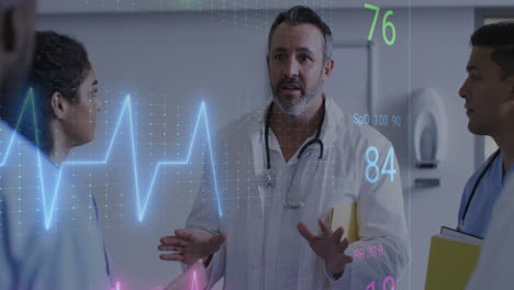 Animation-Eines-Herzfrequenzmessers-über-Einem-Gemischtrassigen-Männlichen-Arzt,-Der-Mit-Seinem-Team-Im-Krankenhaus-Diskutiert