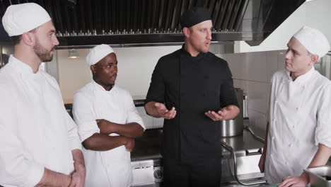 Diverse-male-chef-instructing-group-of-trainee-male-chefs-in-kitchen,-slow-motion