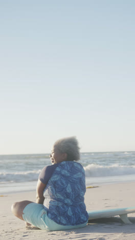 Vertikales-Video-Einer-Glücklichen-älteren-Afroamerikanerin,-Die-Am-Strand-Sitzt,-In-Zeitlupe