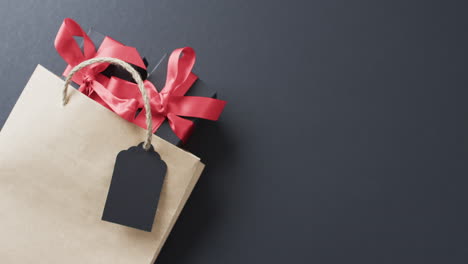 A-brown-paper-gift-bag-with-a-vibrant-red-ribbon-and-a-blank-tag-lies-on-a-dark-surface,-with-copy-s