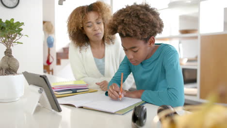 Glückliche-Afroamerikanische-Mutter-Hilft-Ihrem-Sohn-Bei-Den-Hausaufgaben-Mit-Einem-Tablet-In-Der-Küche,-Zeitlupe