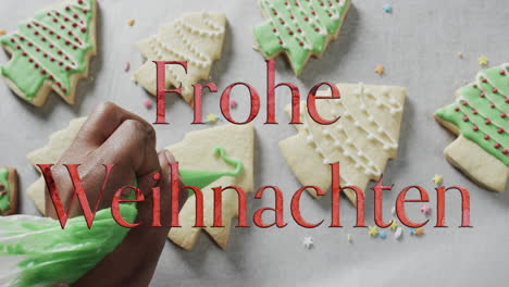 Frohe-weihnachten-text-in-red-over-caucasian-hand-decorating-christmas-cookies-on-white-background