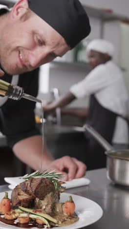 Focused-caucasian-male-chef-pouring-olive-oil-on-prepared-meal-in-kitchen,-slow-motion,-vertical