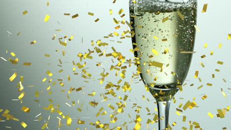 Animation-Von-Goldenem-Konfetti,-Das-Vor-Grauem-Hintergrund-über-Ein-Champagnerglas-Fällt