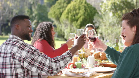 Happy-diverse-male-and-female-friends-toasting-on-celebration-meal-in-sunny-garden