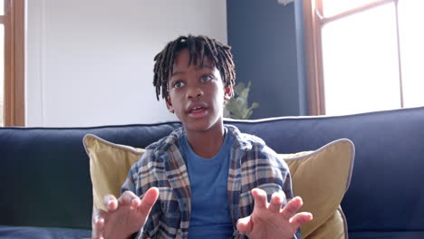 Niño-Afroamericano-Sentado-En-Un-Sofá-Teniendo-Videollamada-En-Casa,-Cámara-Lenta