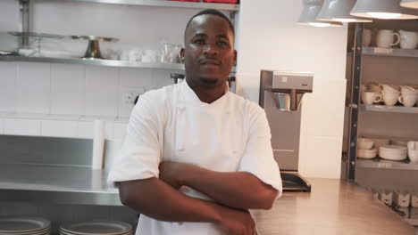 Portrait-of-happy-african-american-male-chef-crossing-arms-and-smiling-in-kitchen,-slow-motion