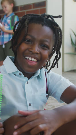 Video-of-happy-african-american-boy-holding-books-in-front-of-school