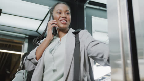 Fröhliche-Afroamerikanische-Geschäftsfrau,-Die-Im-Aufzug-Auf-Dem-Smartphone-Spricht,-Zeitlupe