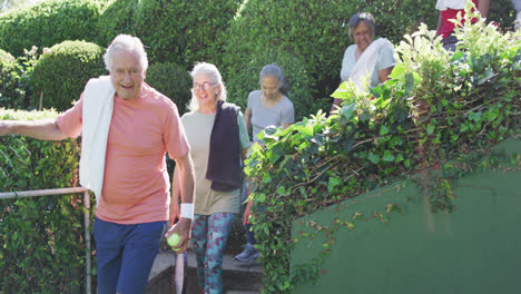 Diverse-group-of-happy-male-and-female-seniors-arriving-at-sunny-outdoor-tennis-court,-slow-motion