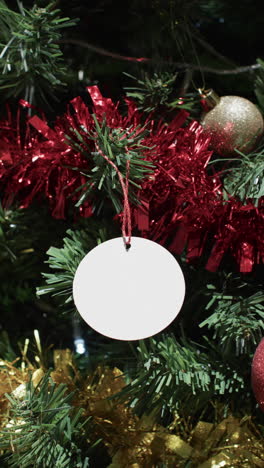 Vertical-video-of-christmas-tree-withdecorations-and-white-tag-with-copy-space