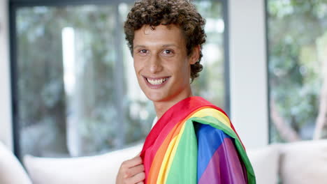 Portrait-of-happy-biracial-man-holding-rainbow-lgbt-flag-at-home,-slow-motion