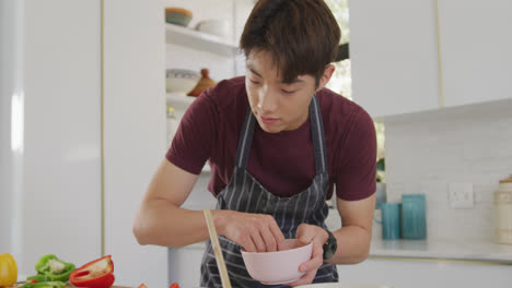 Asian-boy-wearing-apron-preparing-food-in-the-kitchen-at-home