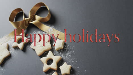 Happy-holidays-text-in-red-over-christmas-cookies-and-bow-on-grey-background