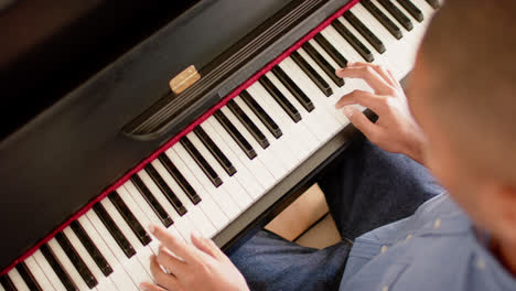 High-angle-view-of-biracial-man-playing-piano-at-home,-slow-motion