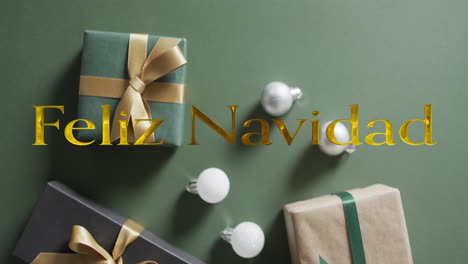 Feliz-navidad-text-in-gold-over-christmas-baubles-and-presents-on-green-background
