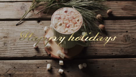Happy-holidays-text-in-gold-over-christmas-hot-chocolate-with-marshmallows-on-wooden-background