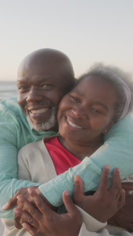 Vertical-video-of-senior-african-american-couple-embracing-at-beach,-in-slow-motion