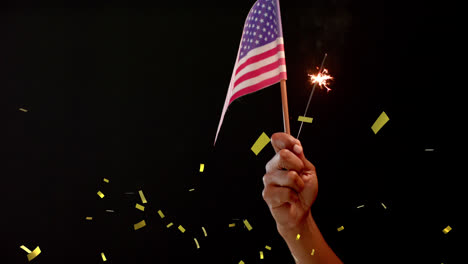 Animation-of-confetti-falling-over-hand-holding-flag-of-united-states-of-america-and-sparkler