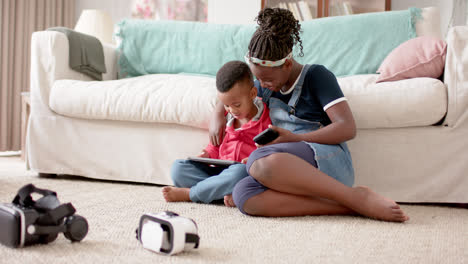 African-american-sister-and-brother-using-tablet-and-smartphone-in-living-room,-slow-motion