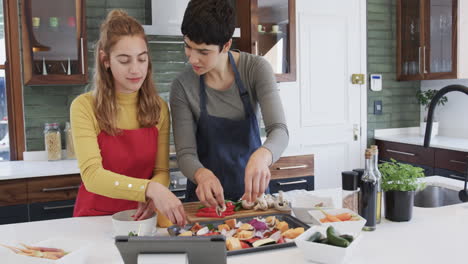 Happy-caucasian-lesbian-couple-preparing-food-and-using-tablet-in-sunny-kitchen