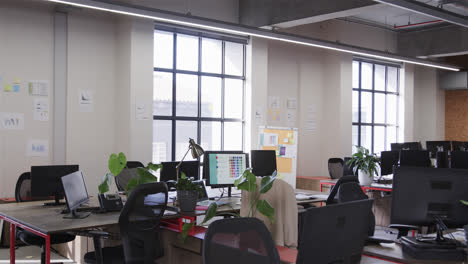 Office-workspace-with-large-windows,-chairs-and-desks-with-computers,-lamps-and-plants,-slow-motion