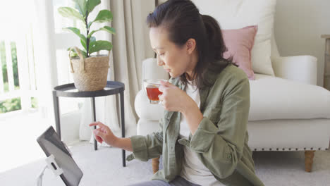 Happy-asian-woman-drinking-tea-and-using-tablet-in-bedroom,-in-slow-motion