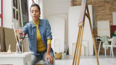Biracial-woman-selects-paintbrushes-in-a-bright-studio