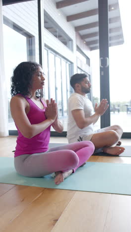 Video-Vertical-De-Una-Pareja-Birracial-Haciendo-Yoga-Y-Meditando-En-Casa,-En-Cámara-Lenta