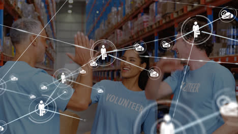 Animation-of-network-of-connections-with-icons-over-diverse-volunteers-high-fiving-in-warehouse