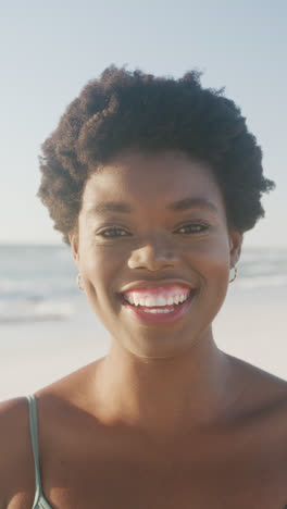 Vertical-video-of-portrait-of-happy-african-american-woman-smiling-at-beach,-in-slow-motion