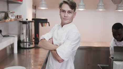 Portrait-of-happy-caucasian-male-chef-crossing-arms-and-smiling-in-kitchen,-copy-space,-slow-motion