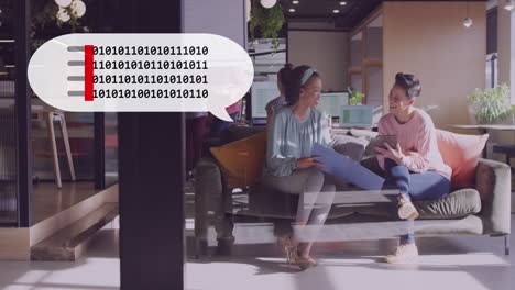 Animation-of-binary-coding-on-a-speech-bubble-against-two-diverse-women-discussing-at-office