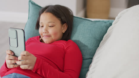 Video-Eines-Glücklichen-Asiatischen-Mädchens,-Das-Mit-Seinem-Smartphone-Auf-Dem-Sofa-Ruht
