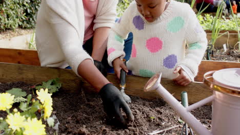 Glückliche-Afroamerikanische-Großmutter-Und-Enkelin-Bei-Der-Gartenarbeit,-Familie-Im-Hintergrund,-Zeitlupe