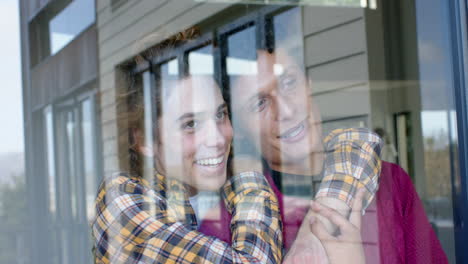Happy-diverse-gay-male-couple-looking-through-window-and-embracing-at-home,-slow-motion