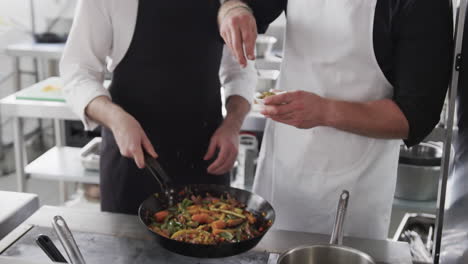 Caucasian-male-chef-instructing-trainee-male-chef-in-kitchen,-slow-motion