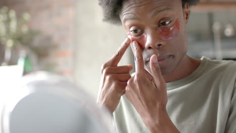 African-american-man-sitting-on-sofa,-applying-under-eye-patches-at-home,-slow-motion