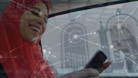 Animation-Von-Punkten,-Die-Mit-Linien-über-Einer-Lächelnden-Jungen-Frau-Im-Hijab-Verbunden-Sind,-Die-Im-Auto-Ein-Mobiltelefon-Benutzt