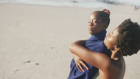 Happy-african-american-mother-and-daughter-embracing-at-beach,-in-slow-motion,-with-copy-space