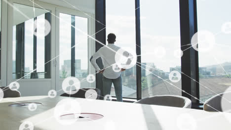 Animation-of-network-of-profile-icons-against-rear-view-of-man-looking-out-of-window-at-office