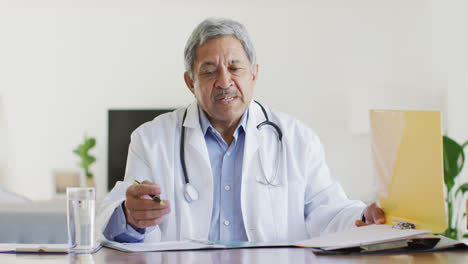Senior-biracial-male-doctor-talking-and-gesturing-during-video-consultation