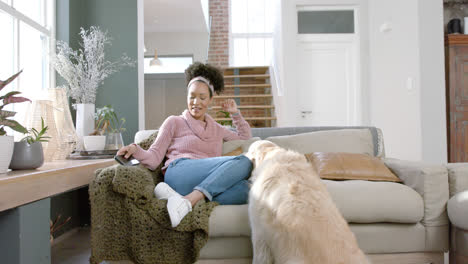 Happy-biracial-woman-petting-golden-retriever-dog-and-using-smartphone-at-home,-slow-motion