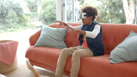 African-american-boy-sitting-on-sofa,-using-vr-headset-and-touching-virtual-screen,-slow-motion