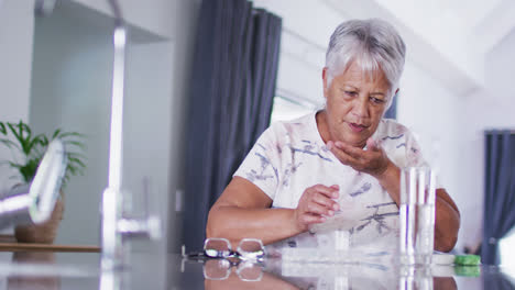 Ältere-Frau-Mit-Gemischter-Abstammung-Mit-Glas-Wasser,-Die-Tabletten-Einnimmt